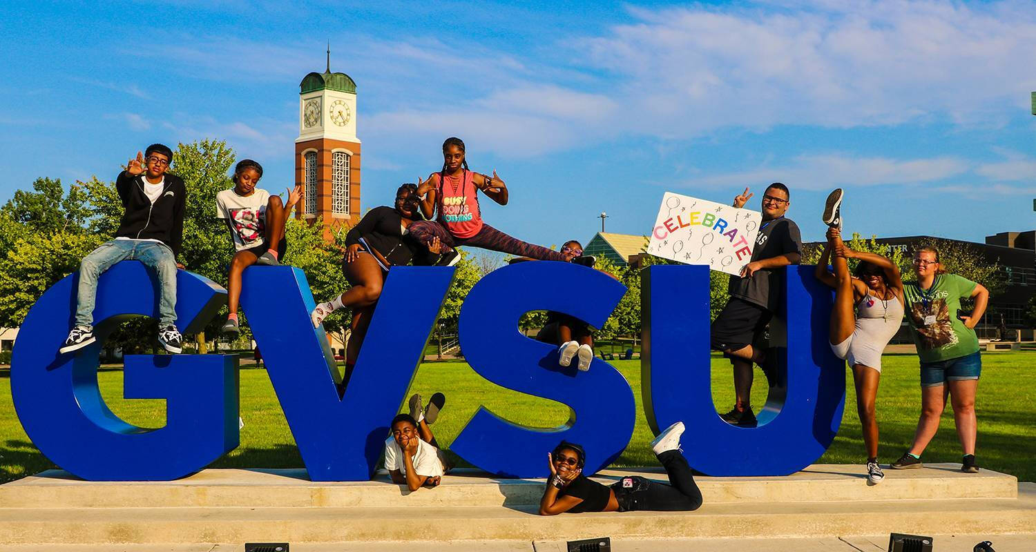 Students sitting on the GVSU letters with the Cook-Carlton Clocktower in the background